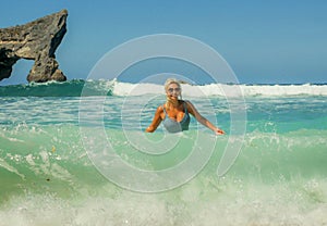 Young happy and sexy blond woman in bikini playing with waves in the sea at stunning beautiful tropical beach enjoying carefree