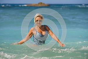 Young happy and sexy blond woman in swimsuit bikini playing with waves in the sea at stunning beautiful tropical beach enjoying