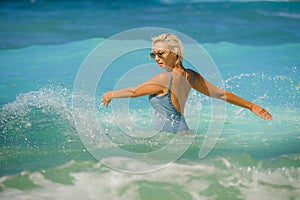 Young happy and sexy blond woman in swimsuit bikini playing with waves in the sea at stunning beautiful tropical beach enjoying