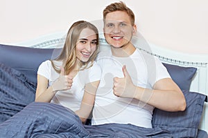 Young happy smile couple lying in bed and show like sign. Loving family concept