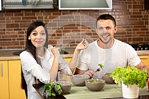 Young happy smiling amorous couple cooking together at home. Man and woman sitting at the table, talking