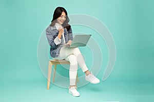Young happy smiling Asian woman holding laptop computer and sitting on chair  on green background.