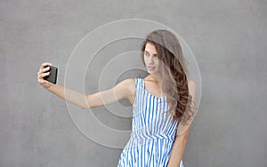 Young happy smiling beautiful woman in light dress with long brunette curly hair posing against wall on a warm