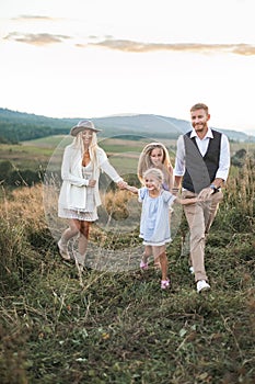 Young happy smiling family with two daughters having fun at countryside, walking in the field, holding hands and talking