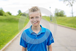 Young happy smiling male boy teenager blond child outside in summer sunshine wearing a blue sweatshirt