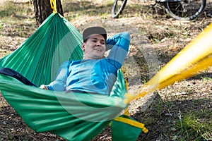 Young happy smiling man in hat relaxing outside in hammock in forest.