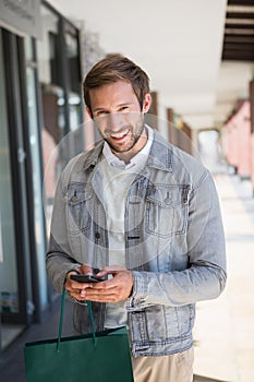 Young happy smiling man holding shopping bags and his mobile