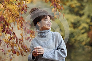 Young happy smiling mixed-race woman with coffee cup in autumn nature