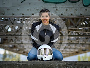 Young happy smiling pretty female motorcyclist posing on a bridge