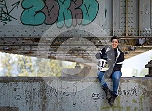 Young happy smiling pretty female motorcyclist posing on a bridge