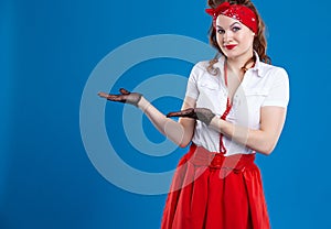 A young happy smiling woman dressed in pin-up style showing something or a copyspace area for a text or slogan