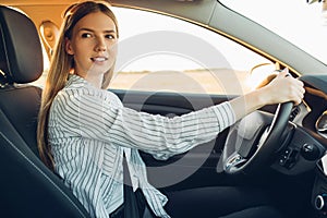 Young happy smiling woman driving her new car at sunset