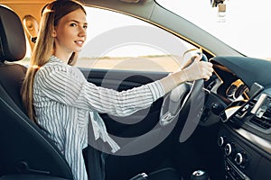 Young happy smiling woman driving her new car at sunset