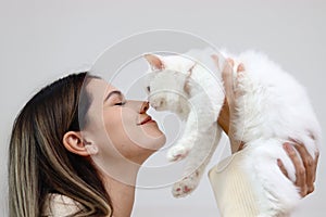 Young happy smiling woman holding cute white Persian cat and lift up her cat, try to kiss her pet, happy beautiful lady playing