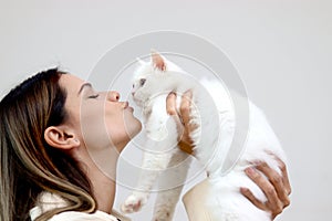 Young happy smiling woman holding cute white Persian cat and lift up her cat, try to kiss her pet, happy beautiful lady playing