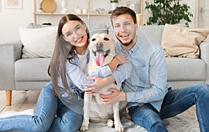 Young happy spouses with dog sitting in living room