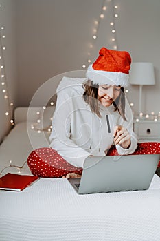 Young happy teen girl in red santa hat shopping online buying Christmas gifts