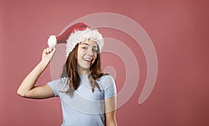 Young happy teenager girl wearing Santa Claus red hat over pink background. Christmas and New Year celebration concept