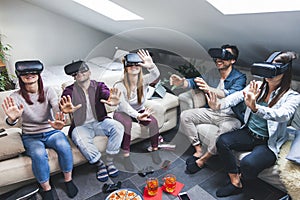 Young happy three friends playing video games virtual reality in their apartment