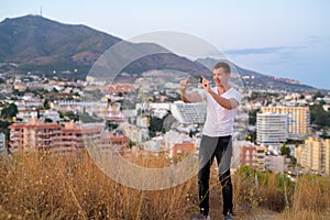 Young Happy Tourist Man Taking Picture With Phone While Standing On Hill Overlooking The City