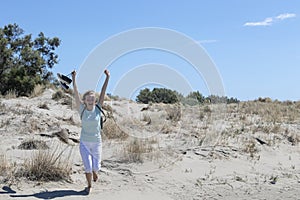 Young happy traveler woman running on the sand dunes coast of Mediterranean sea, beach Beauduc in French Riviera, France