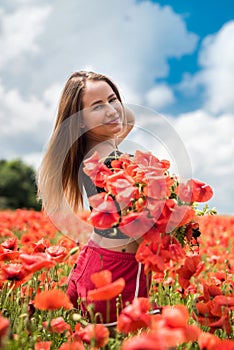 Young happy ukrainian woman holding bouquet of poppies flowers walking, enjoy sunny day in field