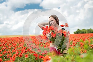 Young happy ukrainian woman holding bouquet of poppies flowers walking, enjoy sunny day in field