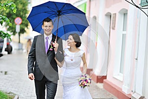 Young happy wedding couple walking by the rain in an old town