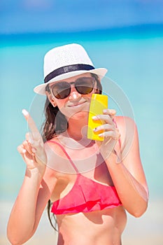 Young happy woman applying suntan lotion on her nose on white beach