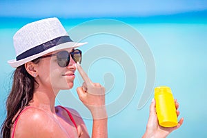 Young happy woman applying suntan lotion on her nose on white beach