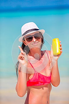 Young happy woman applying suntan lotion on her nose on white beach