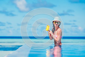 Young happy woman applying suntan lotion on her nose on white beach