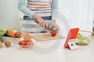 The young happy woman in apron looking at recipe in tablet in the kitchen. Vegetable salad. Dieting concept. Healthy lifestyle.