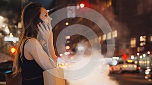 Young happy woman with bags standing in traffic downtown in the evening and talking on mobile phone in new York, America