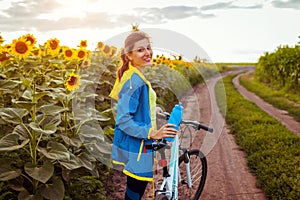 Young happy woman bicyclist riding bicycle in sunflower field. Summer sport activity. Healthy lifestyle