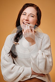 Young happy woman biting gingerbread cookie on yellow background.