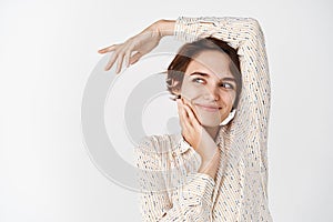 Young happy woman in blouse, posing relaxed and sensual on white background, touching clean soft face and smiling