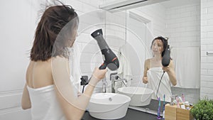 Young happy woman blow drying hair in bathroom, lifestyle. Hair style beauty concept.