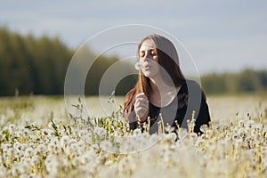 Young happy woman blowing dandelion in a field of dandelions