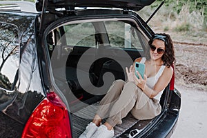 Young happy woman in a car using mobile phone. Travel concept