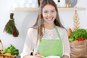 Young happy woman is cooking or eating fresh salad in the kitchen. Food and health concept