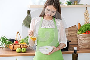 Young happy woman is cooking or eating fresh salad in the kitchen. Food and health concept