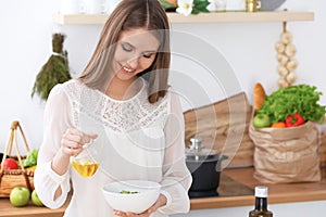 Young happy woman is cooking or eating fresh salad in the kitchen. Food and health concept