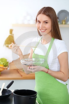 Young happy woman cooking soup in the kitchen. Healthy meal, lifestyle and culinary concept. Smiling student girl