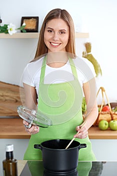 Young happy woman cooking soup in the kitchen. Healthy meal, lifestyle and culinary concept. Smiling student girl