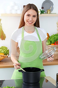 Young happy woman cooking soup in the kitchen. Healthy meal, lifestyle and culinary concept. Smiling student girl