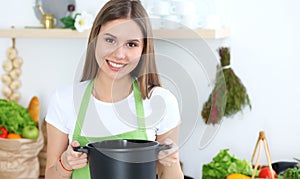 Young happy woman cooking soup in the kitchen. Healthy meal, lifestyle and culinary concept. Smiling student girl