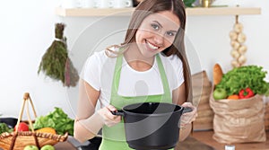 Young happy woman cooking soup in the kitchen. Healthy meal, lifestyle and culinary concept. Smiling student girl