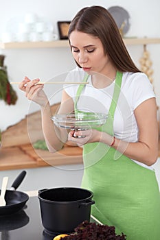 Young happy woman cooking soup in the kitchen. Healthy meal, lifestyle and culinary concept. Smiling student girl