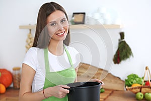 Young happy woman cooking soup in the kitchen. Healthy meal, lifestyle and culinary concept. Smiling student girl